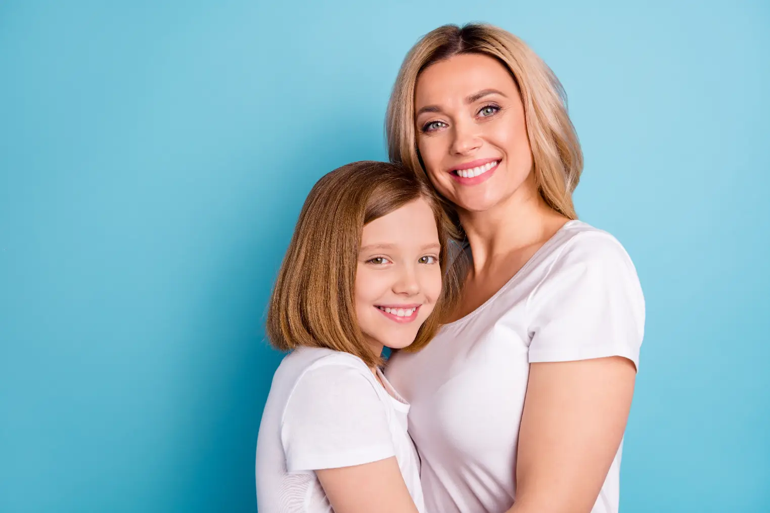 Smiling mother and daughter with smooth, healthy hair against blue background