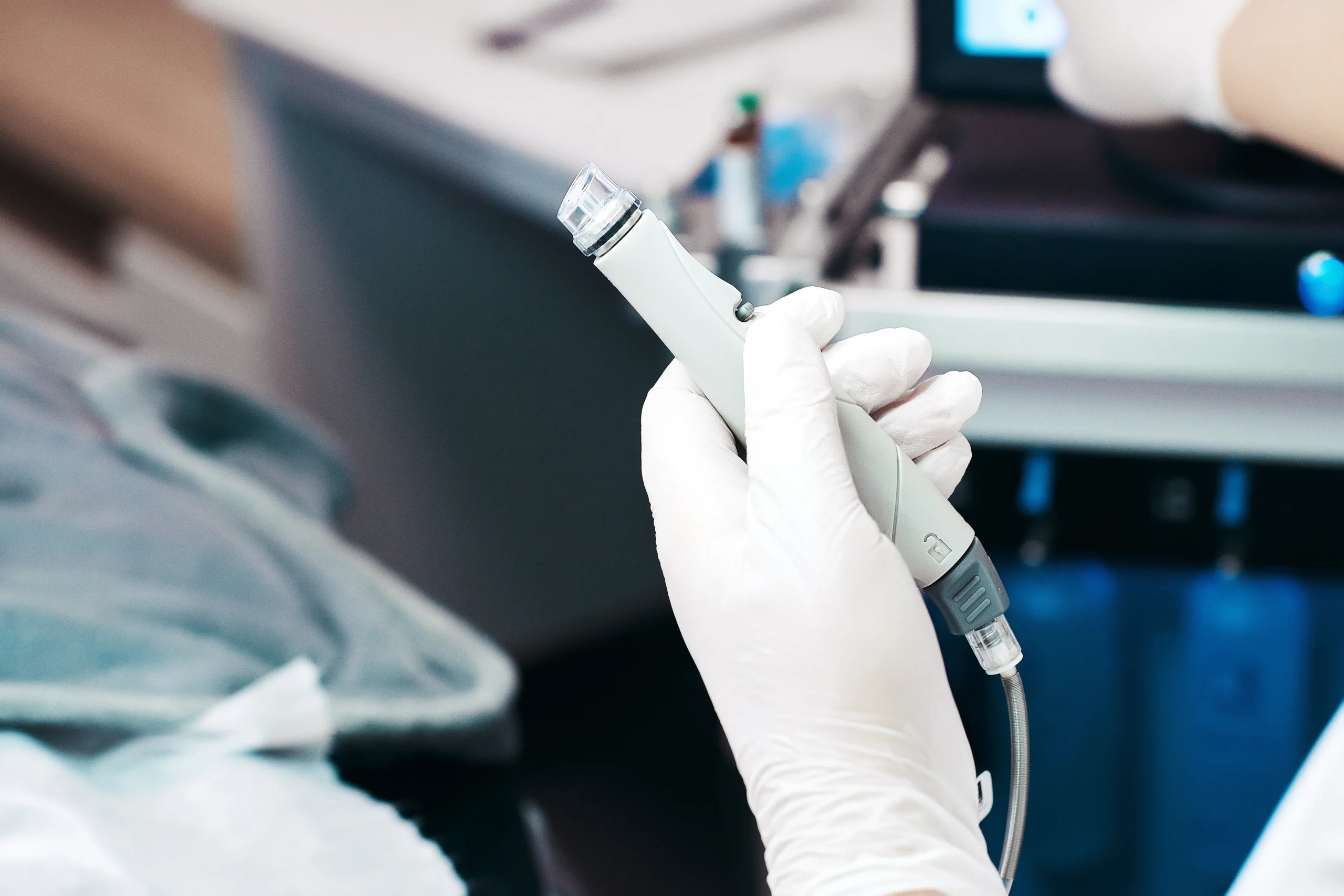 Gloved hand holding microneedling device in clinical setting