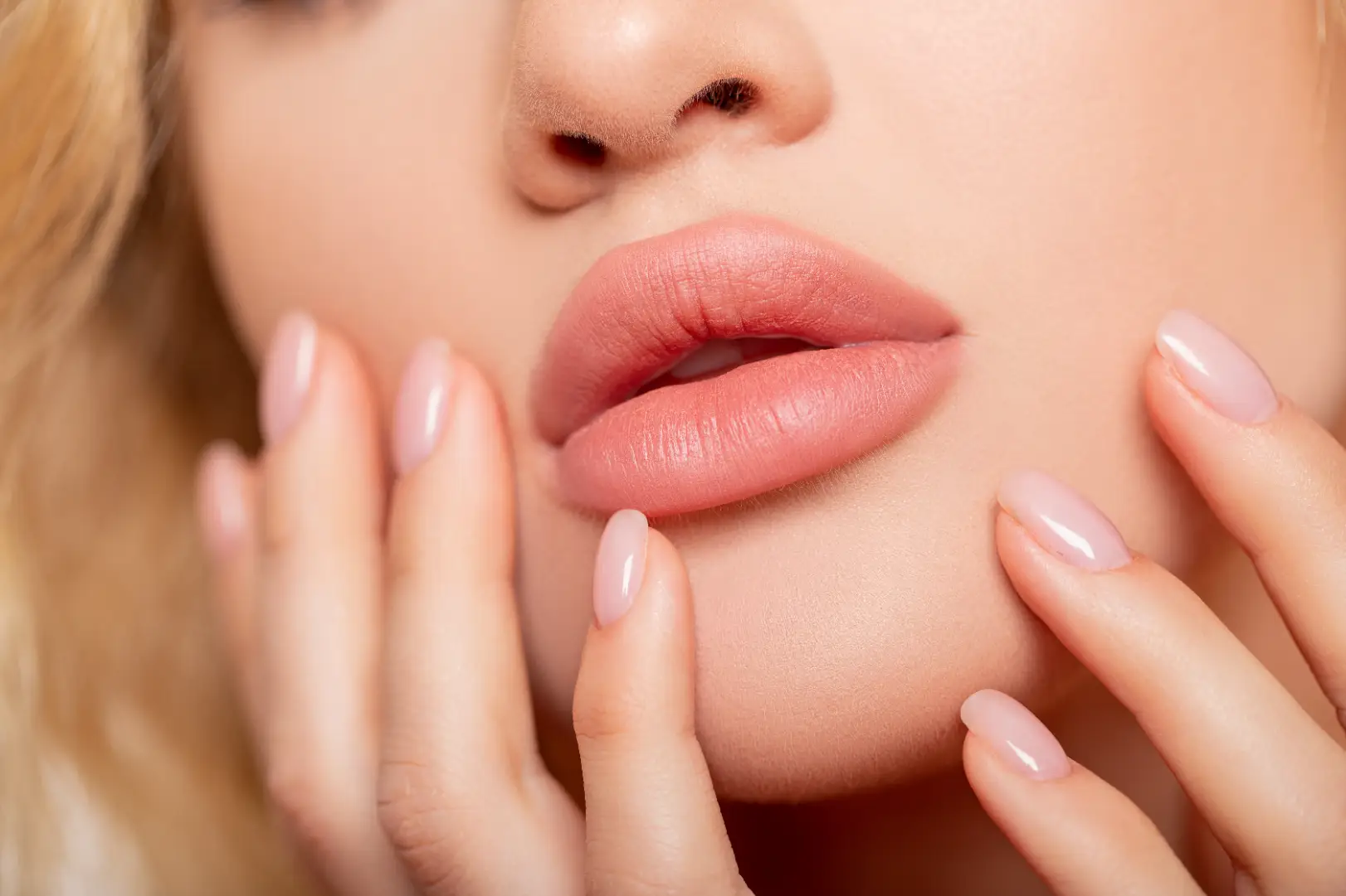 Close-up of lips and lower face with hands gently touching the cheeks.